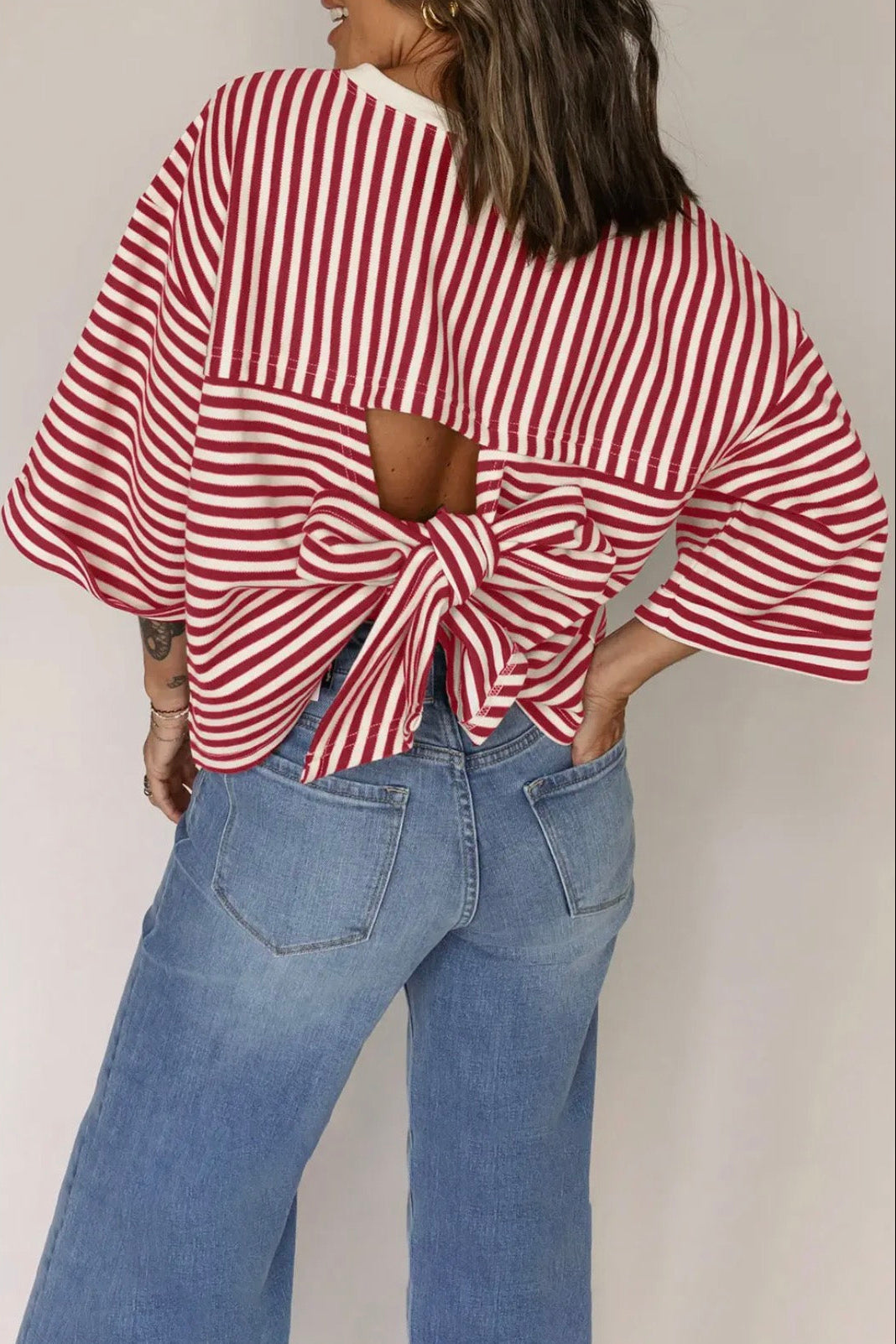 Person wearing a red and white striped top with a bow detail and blue jeans on a plain background